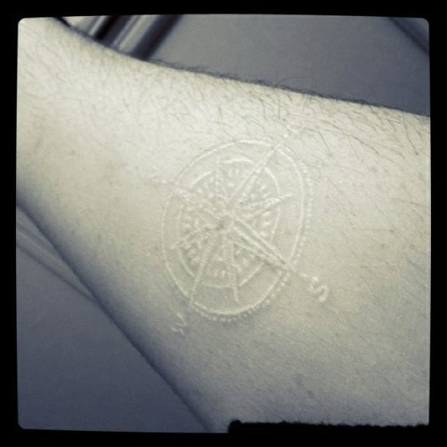Tatuaje en tinta blanca con diseño de brújula en un brazo