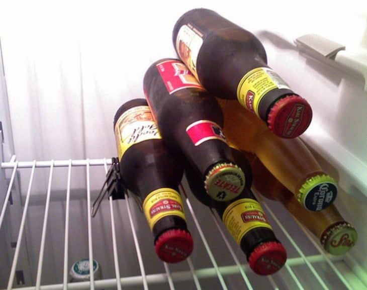 Botellas de cerveza apilas en una pirámide con un clip sujeta papeles en una balda del refrigerador 