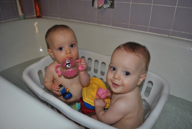 dos bebés dentro de una canasta de plástico dentro de la bañera con juguetes 