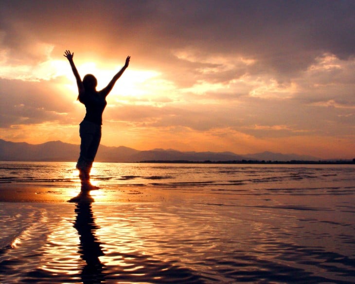 chica estira los brazos, haciendo yoga al atardecer en la playa