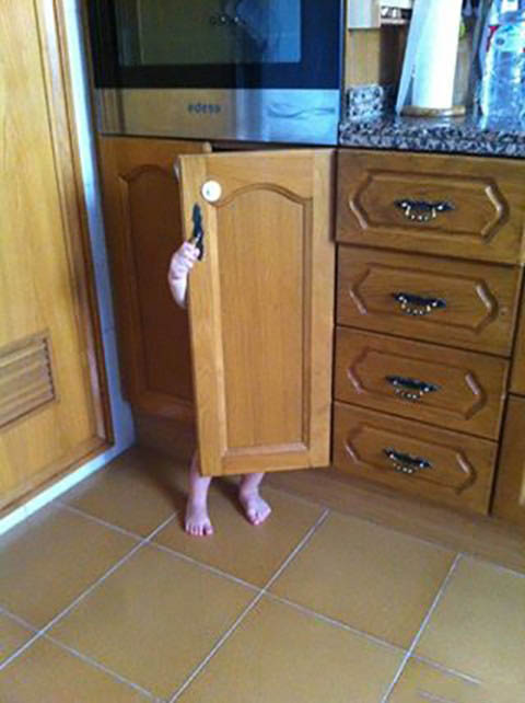 Niño escondido detrás de una puerta de un mueble de madera 