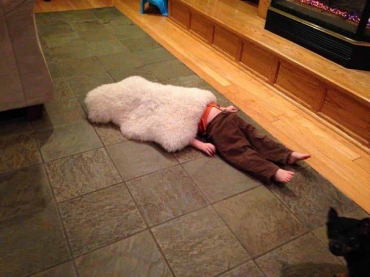 niño acostado en el suelo tapado con un tapete de peluche 