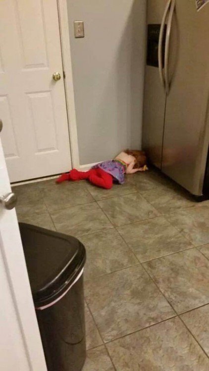 Niña acostada en el suelo frente a un refrigerador 
