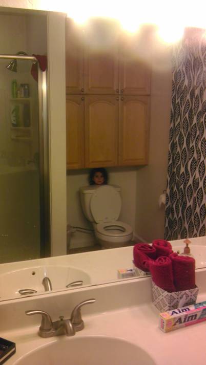 Baño de una casa donde una niña detrás del inodoro