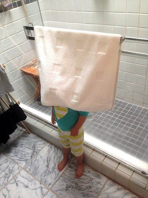 Niña parada en el baño detrás de una toalla 