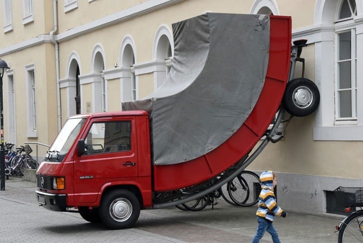 Escultura de un camión doblado hacia arriba en una pared 
