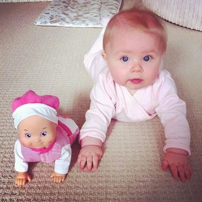 una muñeca junto a una bebe incadas sobre una alfombra 