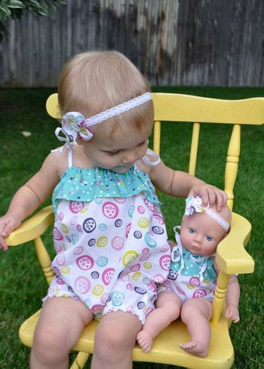 Niña sentada en una mecedora con su muñeca vestidas iguales 