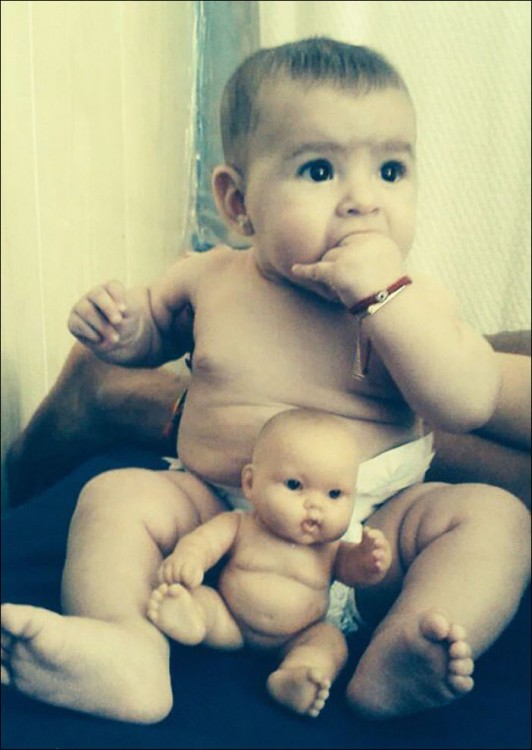 un bebé con su pañal y un pequeño muñeco entre sus piernas 