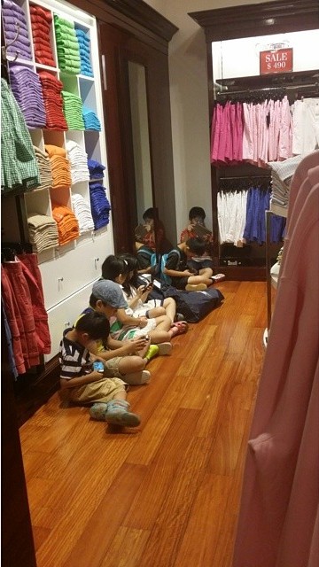 Niños sentados en el suelo en un centro comercial entretenidos con los celulares 
