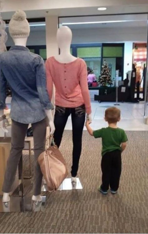 Niño sosteniendo la mano de un maniqui en la puerta del centro comercial