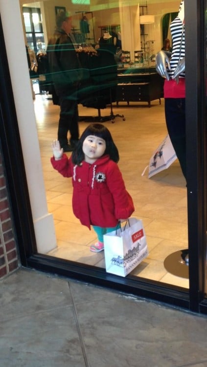 Niña recargada en el vidrio de una tienda de ropa 