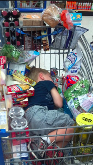 Niño dormido en el carrito del centro comercial en medio de todas las compras 