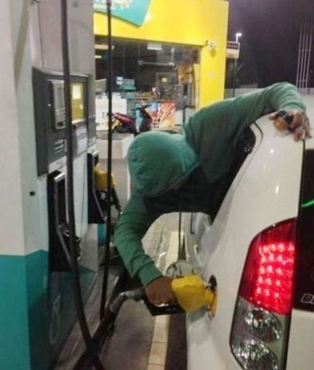 Hombre saliendo por la ventana de un coche despachándose gasolina solo 