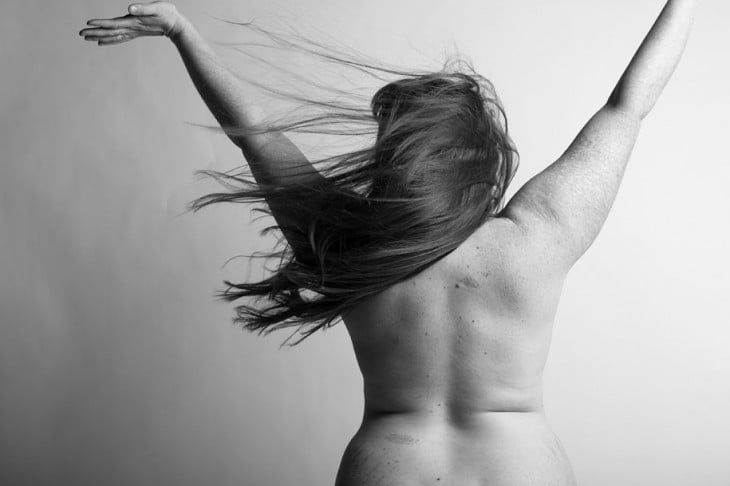 mujer desnuda de espaldas levantando sus manos hacia arriba 