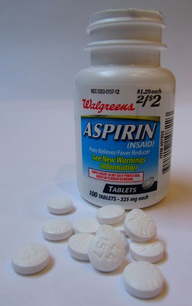 Frasco de pastillas aspirinas con pocas pastillas sueltas frente a él 