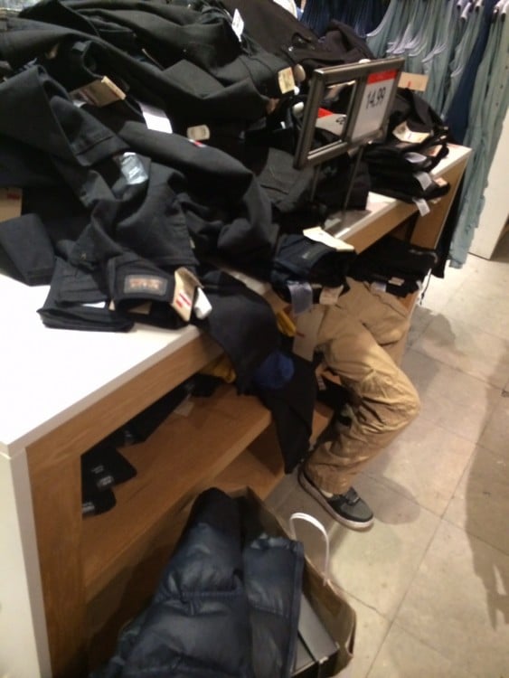 Niño acostado en un estante de pantalones en el centro comercial 