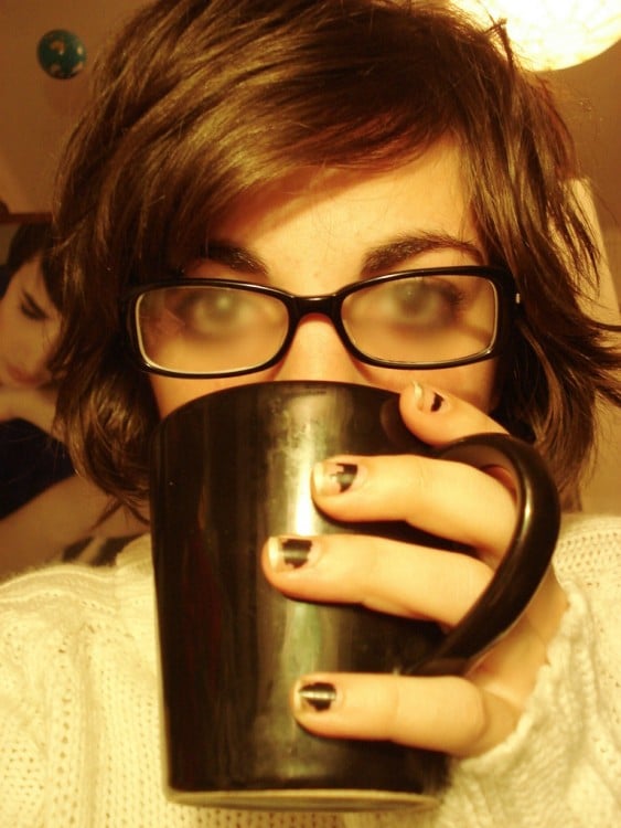 Chica tomando una bebida caliente y con sus lentes empañados 