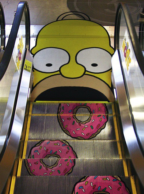 Escaleras eléctricas con forma de donas dirigiéndose hacia una cara de homero Simpson