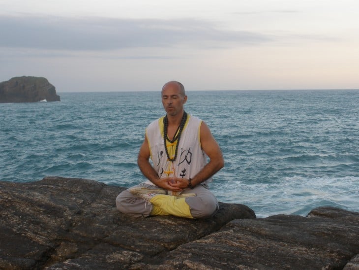 hombre sentado sobre unas rocas frente al mar meditando 