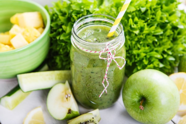 Licuado verde en un frasco de vidrio rodeado de frutas y verduras 