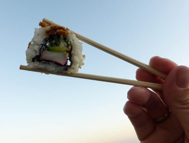 Manos de una persona sosteniendo sushi con palillos chinos 