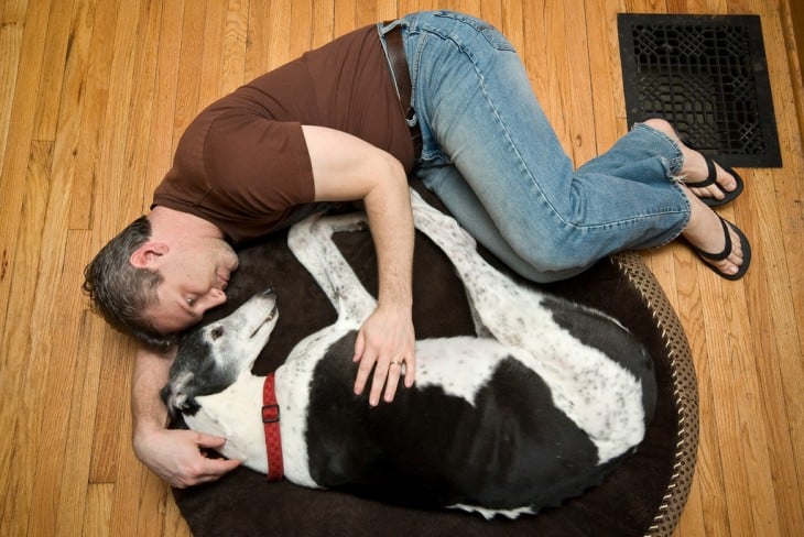 Hombre acostado abrazado de su perro en el suelo de su casa 