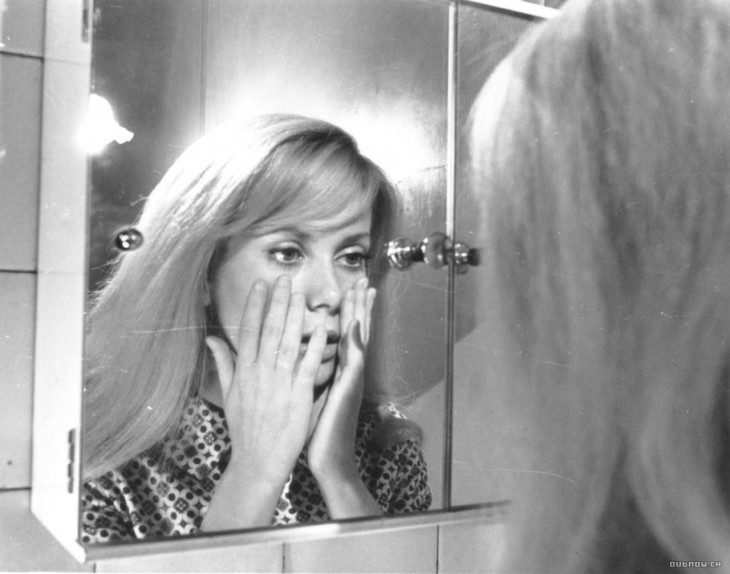 Mujer sosteniendo su cara mientras se ve en el espejo 
