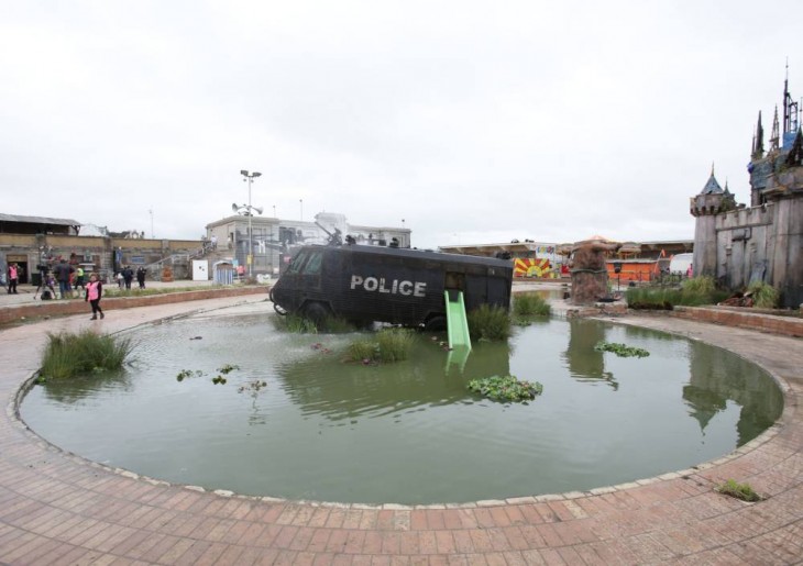 Lago con una camioneta de policía en el centro frente al castillo en el parque Dismaland 