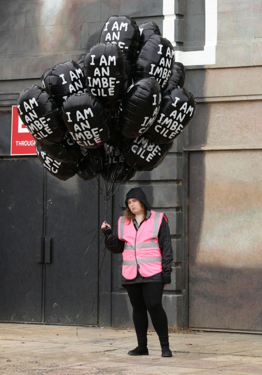Empleada del parque Dismaland con unos globos en color negro con la frase I am an imbecile 
