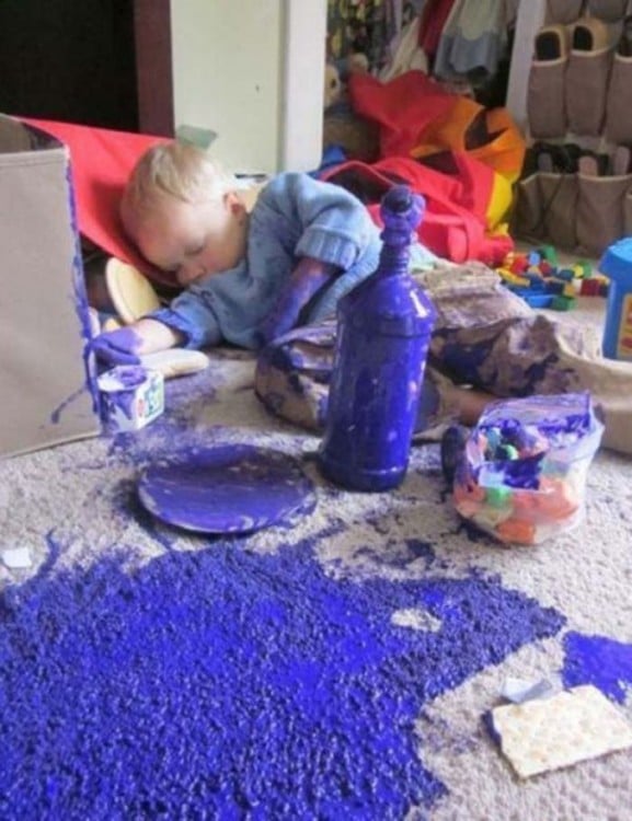 Niño acostado alrededor de muchas cosas en una alfombra llena de pintura 