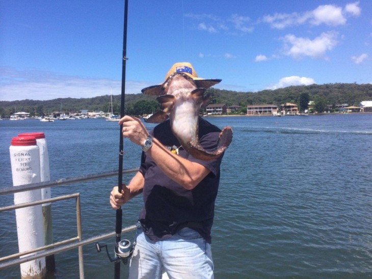 Hombre en el puerto con una caña de pescar y un pez frente a su cara 