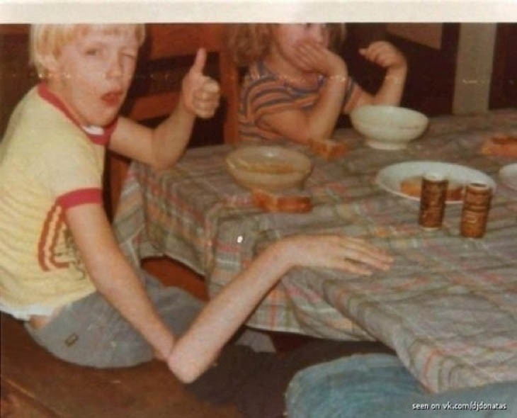 Imagen de personas comiendo en un comedor donde un niño simula tener el brazo muy delgado y largo 