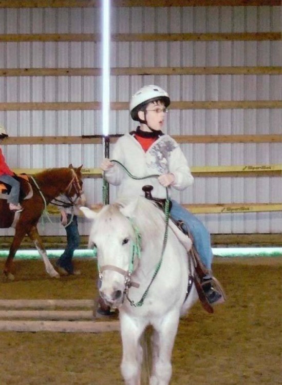 niño montado en un pony en una pose que simula tener un sable de luz en las manos como el de star wars 