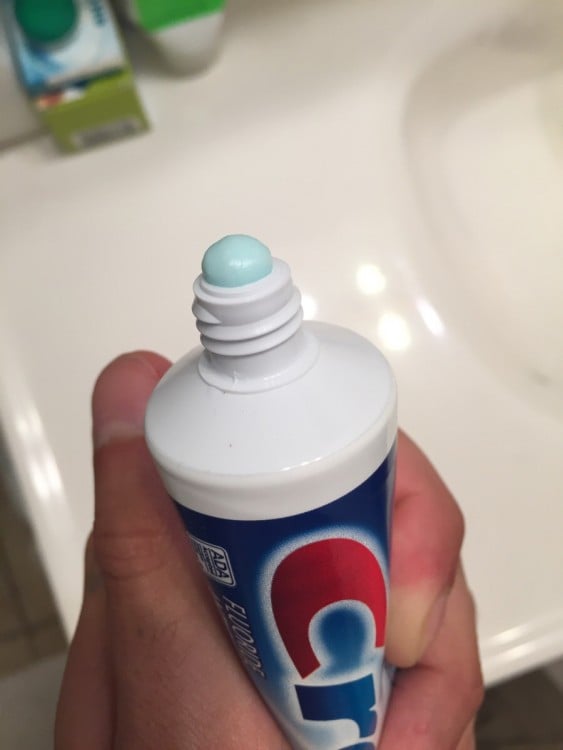 Manos aplastando el tubo de una pasta dental refrescante 