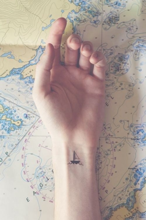 Tatuaje en la muñeca de una mano con el diseño de un pequeño barco navegando 