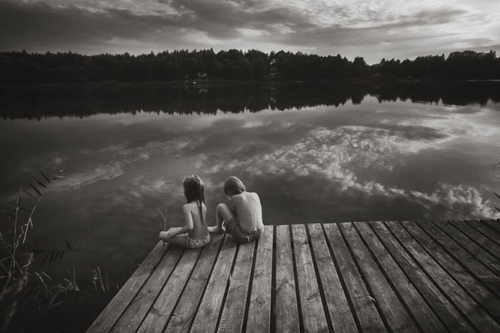 una niña y un niño sentados en un puente a la orilla de un lago 