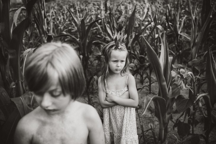 niña con una corona y los brazos cruzados detrás de un niño en medio de unos matorrales 