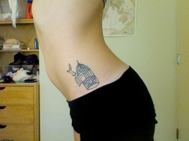 Tatuaje en el costado de una chica con una jaula y un pájaro 