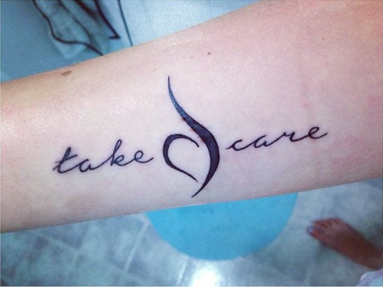 Tatuaje en un brazo con la frase "Take Care" y un símbolo 