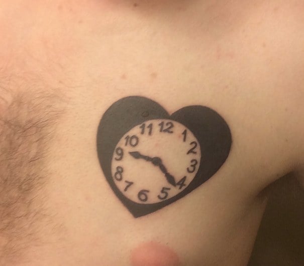 Pecho de un chico con un tatuaje de un reloj en forma de corazón 