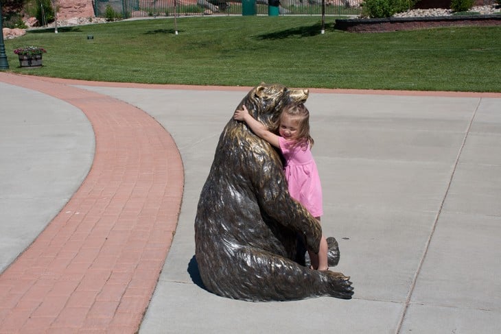 niña abranzando ia un oso de estatua