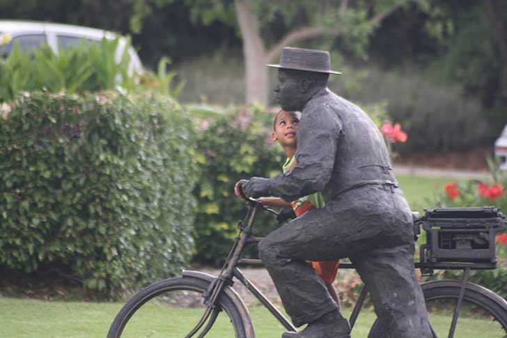 niño montado en una bicicleta junto a una estuatua