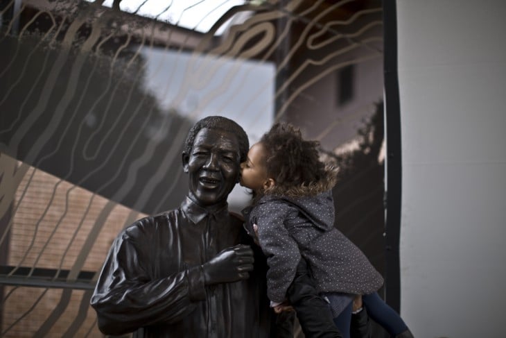 NIÑA DANDOLE UN BESO A LA ESTATUA DE MANDELA