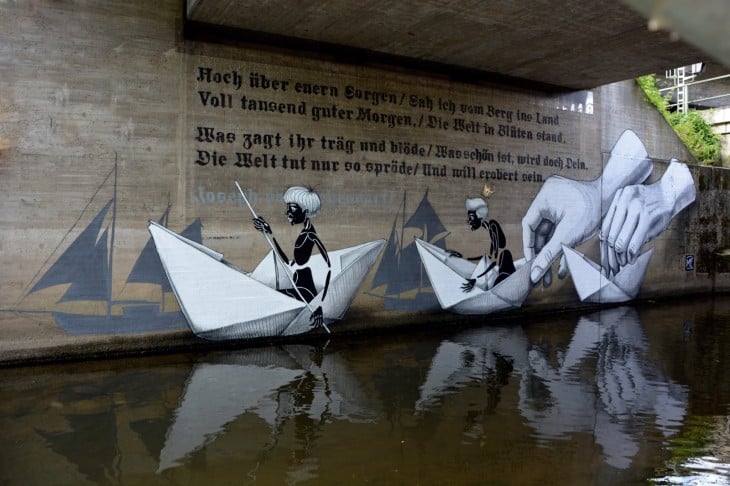 arte urbano en una pared de Alemania donde unos niños van sobre barcos de papel 