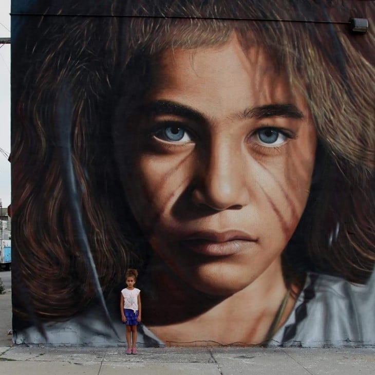 Niña parada frente a una pared que tiene dibujado un rostro de una niña 