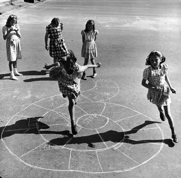 niñas jugando en una calle sobre un avioncito en el suelo 