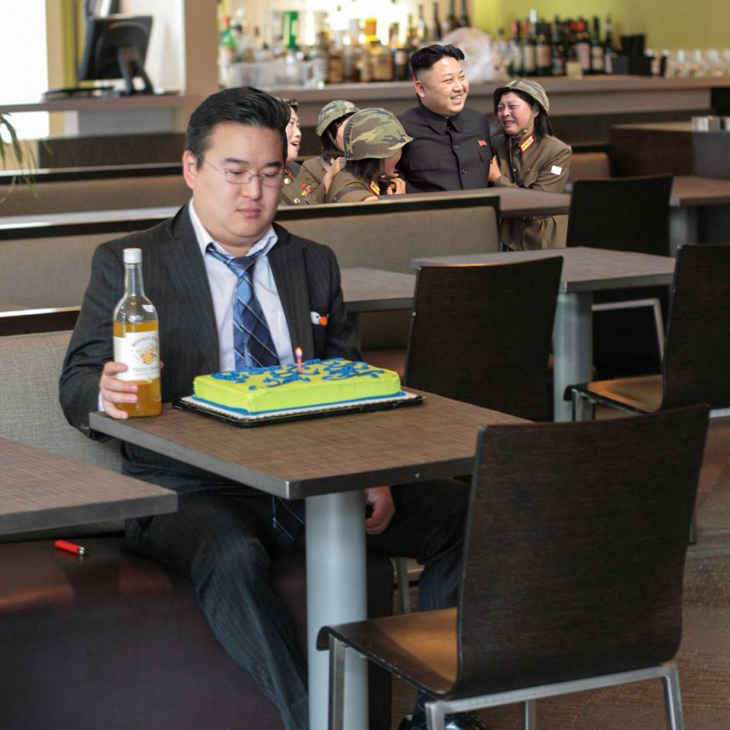 Persona con un pastel solo en la mesa y unas personas abrazándose detrás de él 