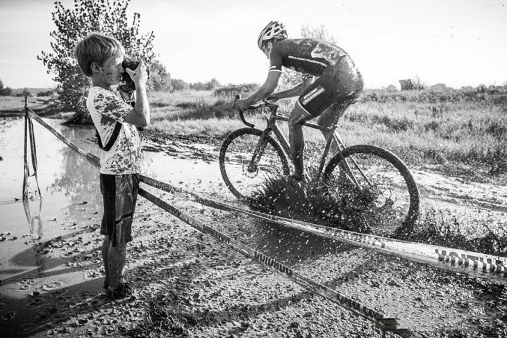 niño tomando una fotografía mientras un ciclista lo salpica de lodo 