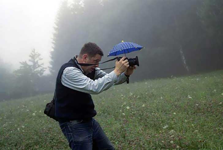 Hombre tomando una fotografía con un pequeño paraguas sobre su cámara 